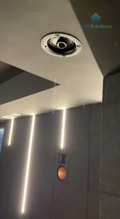 Salle livrée par HomeSolutions : enceinte Atmos au plafond, enceinte murale encastrée, lumières alignées.
